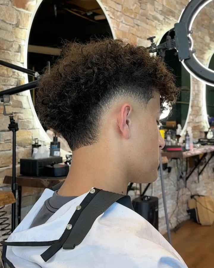 Joven visto de espaldas y de lado con burst fade en cabello afro rizado, curva desvanecida detrás de la oreja