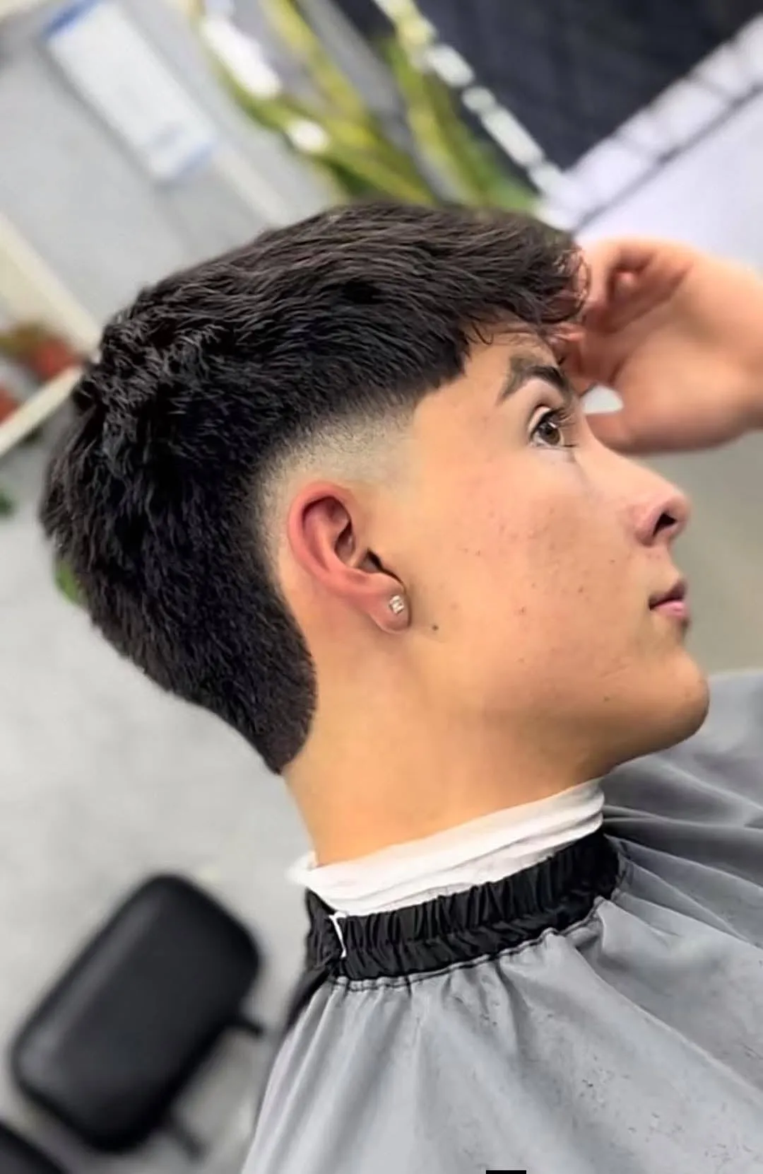 Joven de perfil con burst fade alto que llega casi a la sien y cabello negro lacio con fleco recto sobre la frente