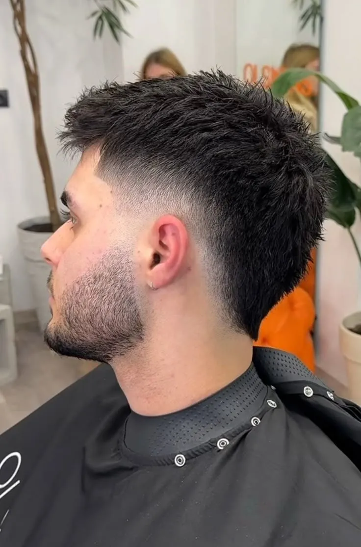 Hombre de perfil con barba completa, burst fade medio y cabello negro texturizado hacia arriba
