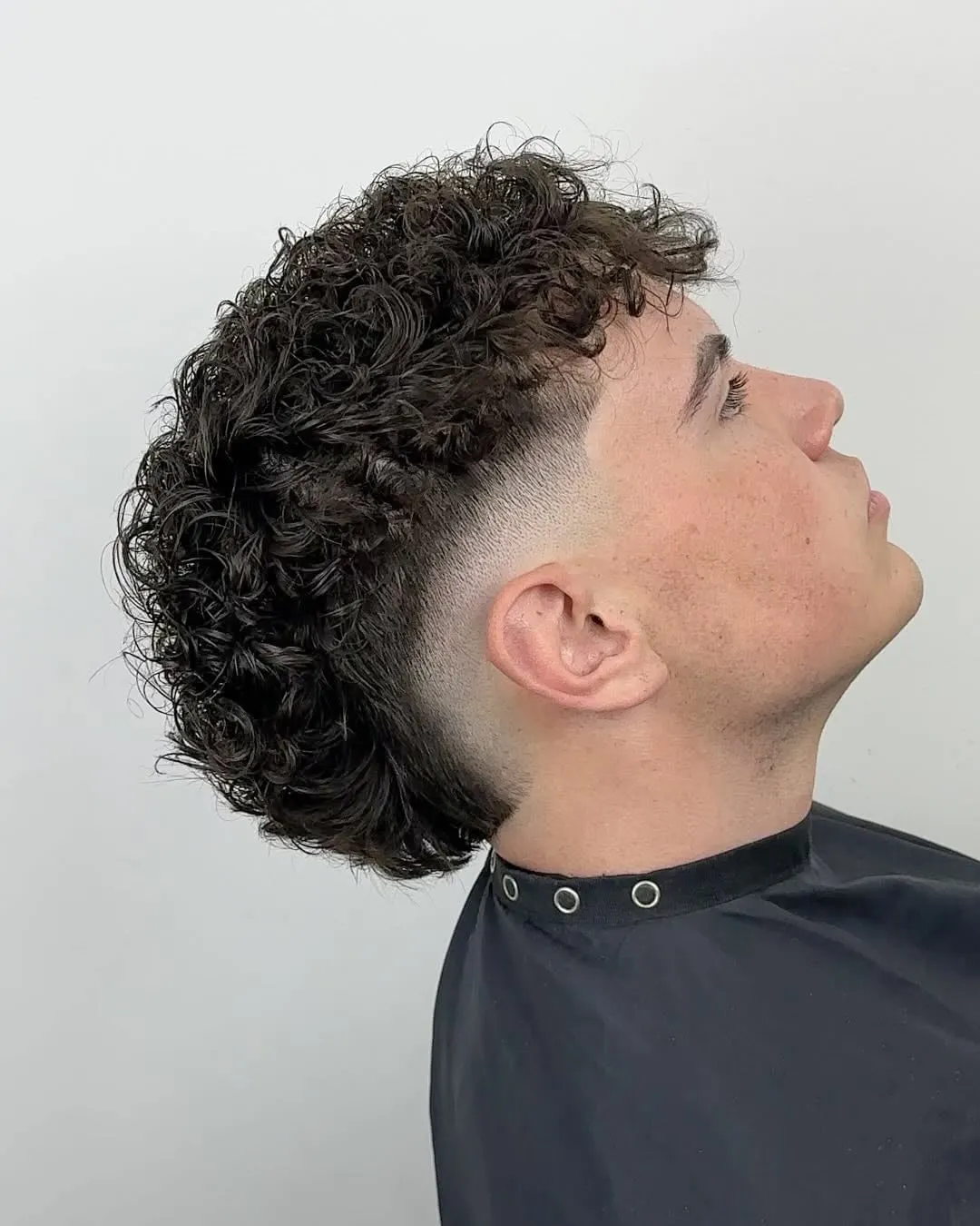 Joven de perfil con burst fade medio y rizos de permanente definidos arriba y en la nuca