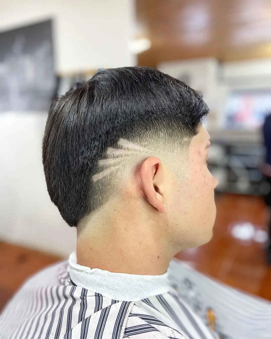 Joven visto de lado con burst fade en cabello negro lacio y varias rayas dibujadas que salen del desvanecido hacia la sien
