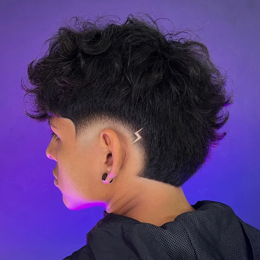 Joven de perfil con burst fade bajo, rizos negros arriba y un pequeño rayo dibujado sobre la oreja