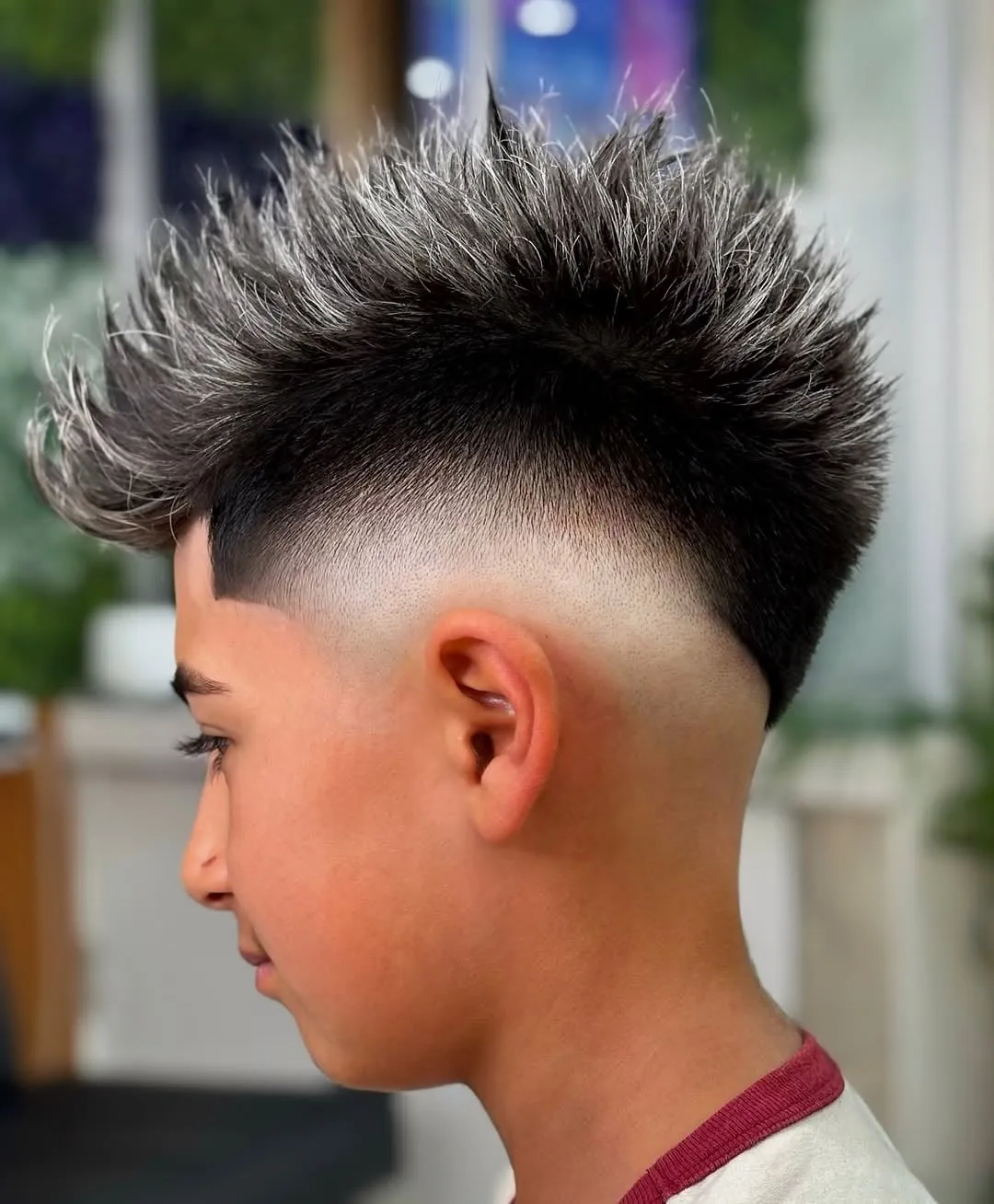 Joven de perfil con burst fade en V, la parte de arriba en puntas levantadas y mechas platinadas en las puntas