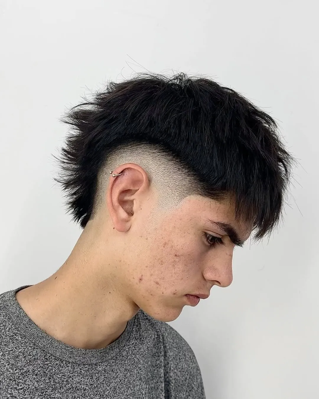 Joven de perfil con burst fade en cabello negro lacio, puntas texturizadas y fleco desordenado hacia la frente