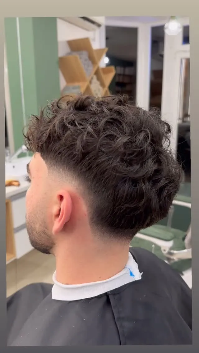 Burst taper fade con desvanecido en semicírculo alrededor de la oreja y cabello ondulado arriba