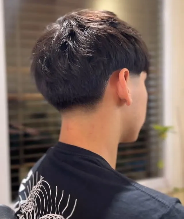 Corte de cabello visto desde atrás con peso arriba, nuca redondeada y taper bajo