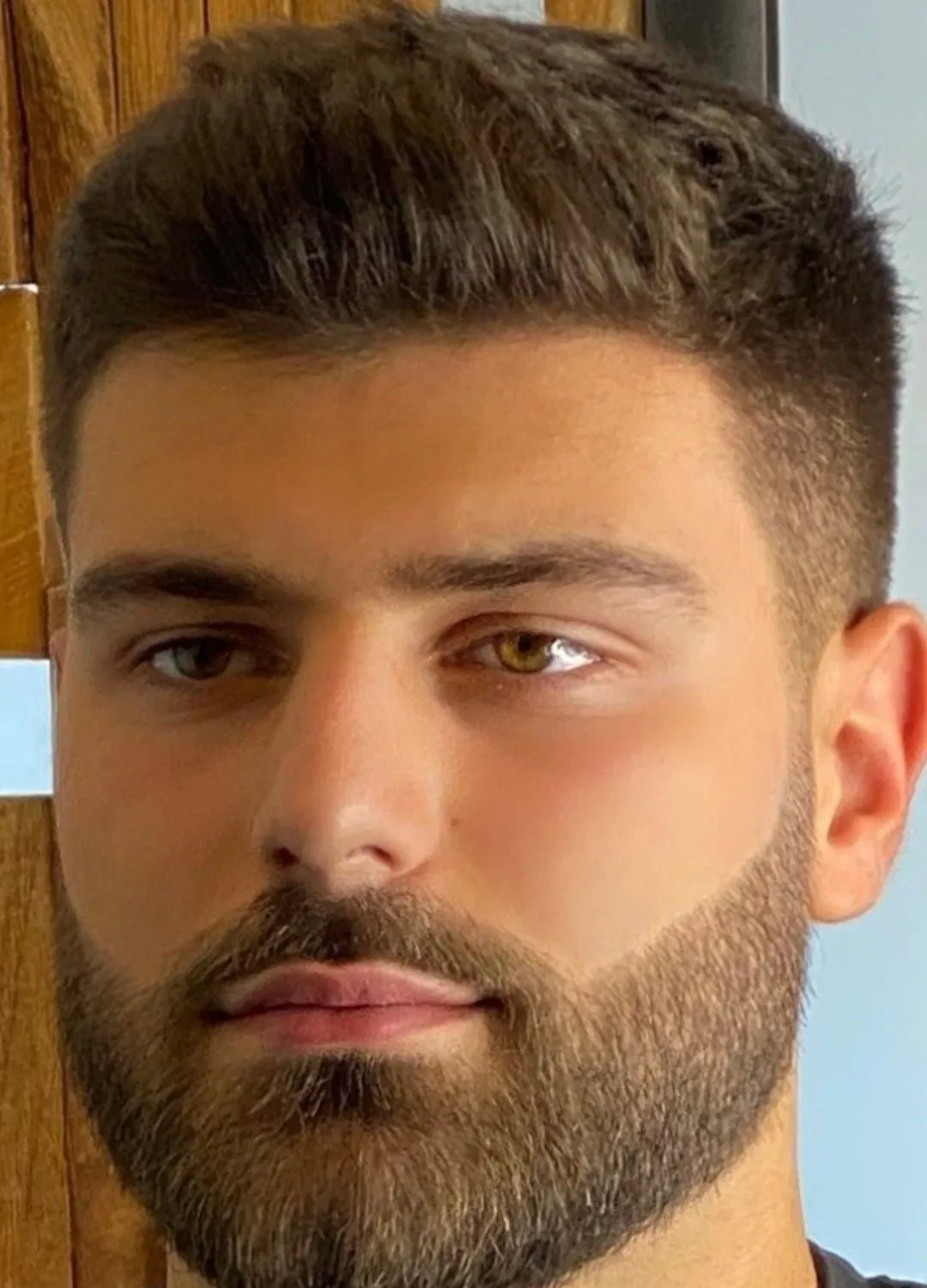 Hombre de frente con corte corto texturizado arriba, lados cortos y barba completa recortada
