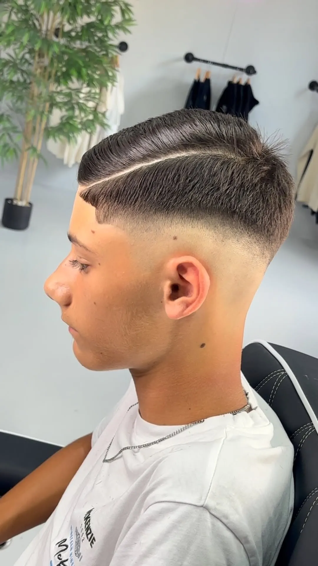 Joven de perfil con corte francés peinado de lado, raya marcada con navaja y mid fade en los lados