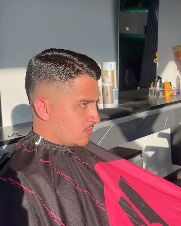 Hombre joven de perfil con corte francés peinado de lado con brillo, high fade en los lados y patilla limpia