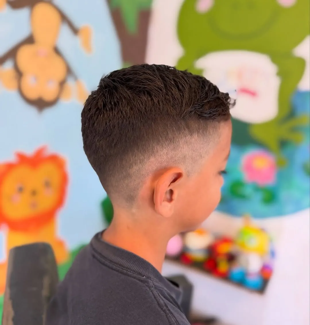 Niño de perfil en una peluquería infantil con desvanecido alto en los costados y cabello castaño oscuro corto y texturizado arriba