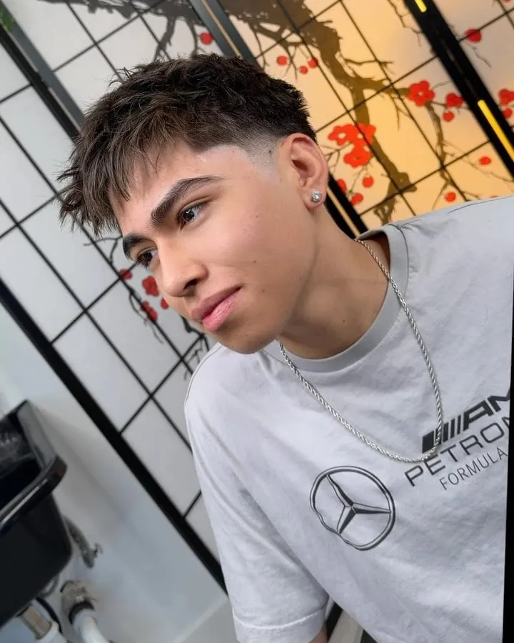 Joven con fleco texturizado que cae sobre la frente y taper fade bajo en una barbería