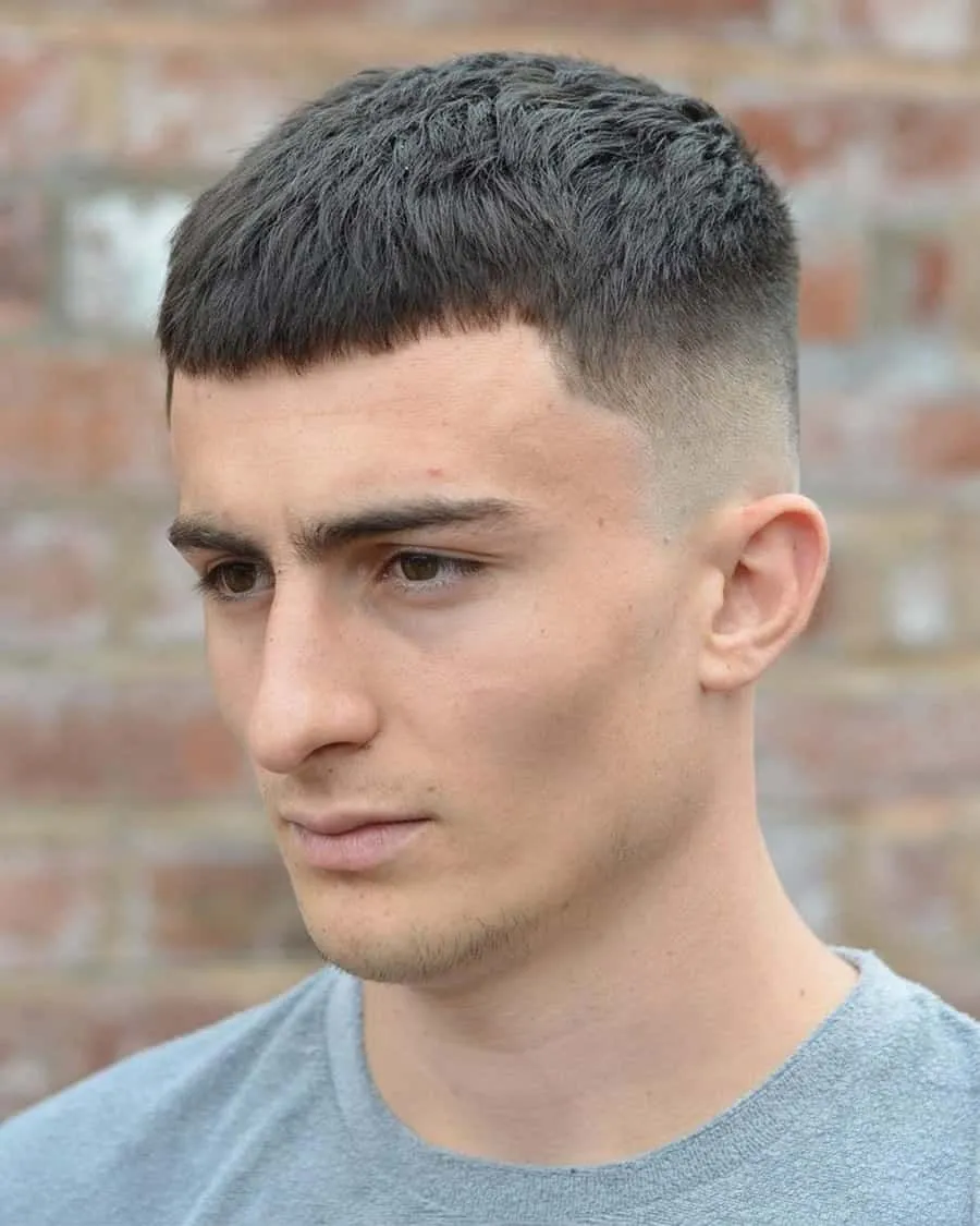 Joven con french crop clásico castaño oscuro, 3 cm arriba, fleco recto bien marcado sobre la frente y fade alto suave