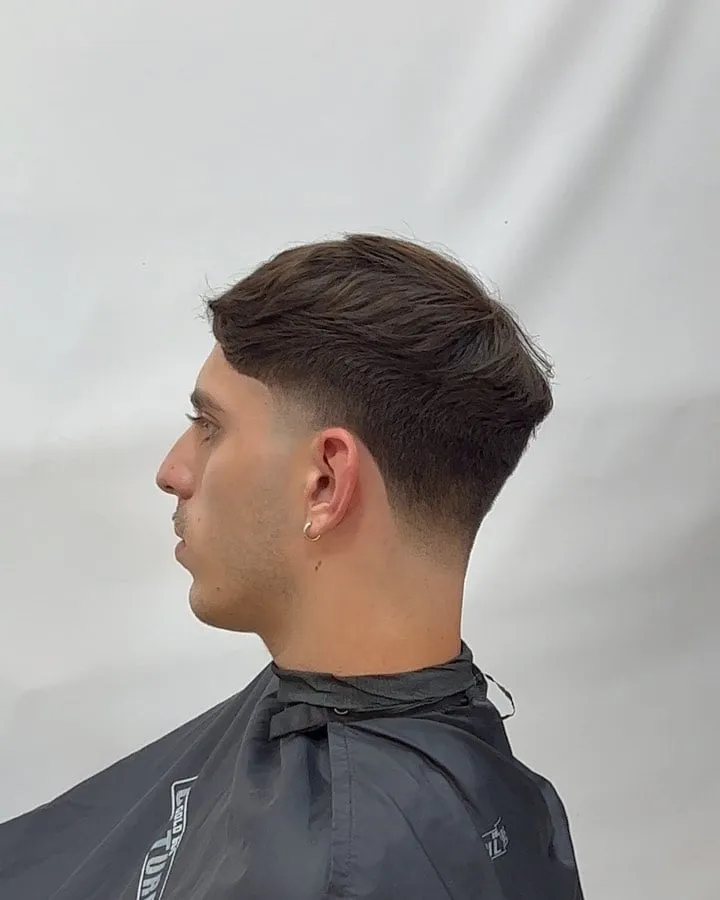 Joven de perfil con french crop castaño, arriba largo con textura suave y taper bajo en la patilla y la nuca