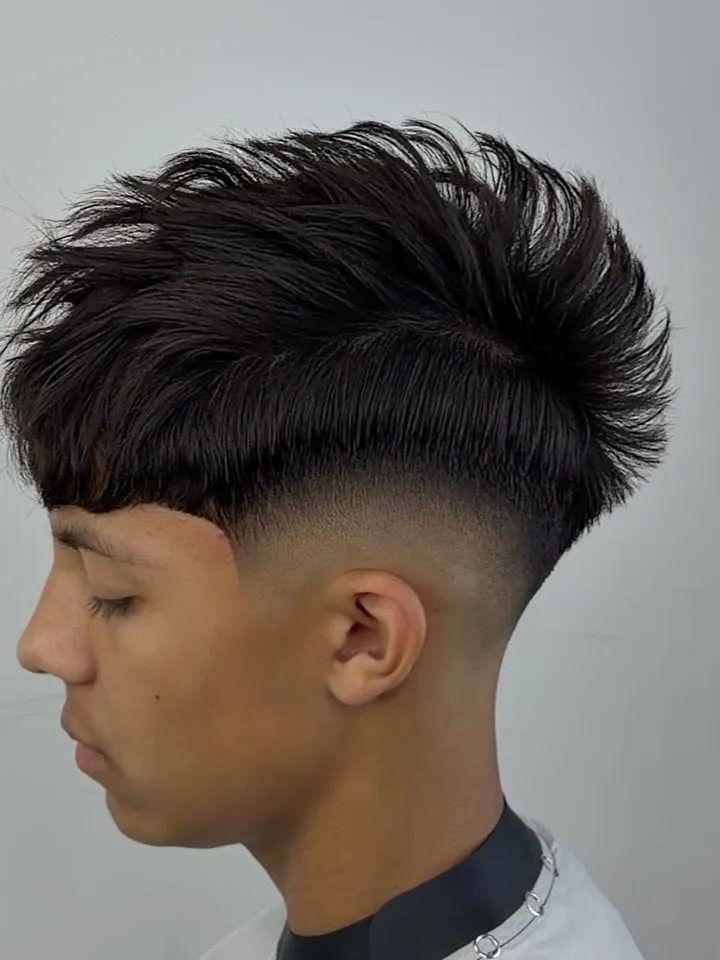 Joven de perfil con french crop negro, puntas largas peinadas hacia arriba, fleco recto debajo y high fade a los lados