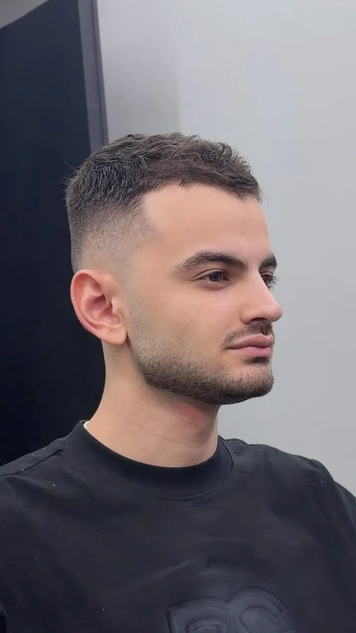Joven de perfil con french crop muy corto, apenas 2 cm de cabello arriba, fleco mínimo y skin fade a la piel