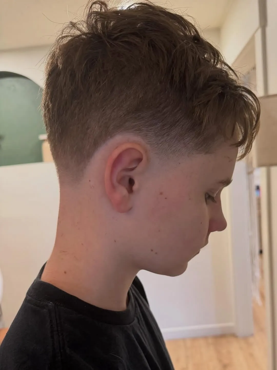 Joven de perfil con french crop castaño claro despeinado, largo arriba con mechones hacia adelante y taper en la sien y la nuca