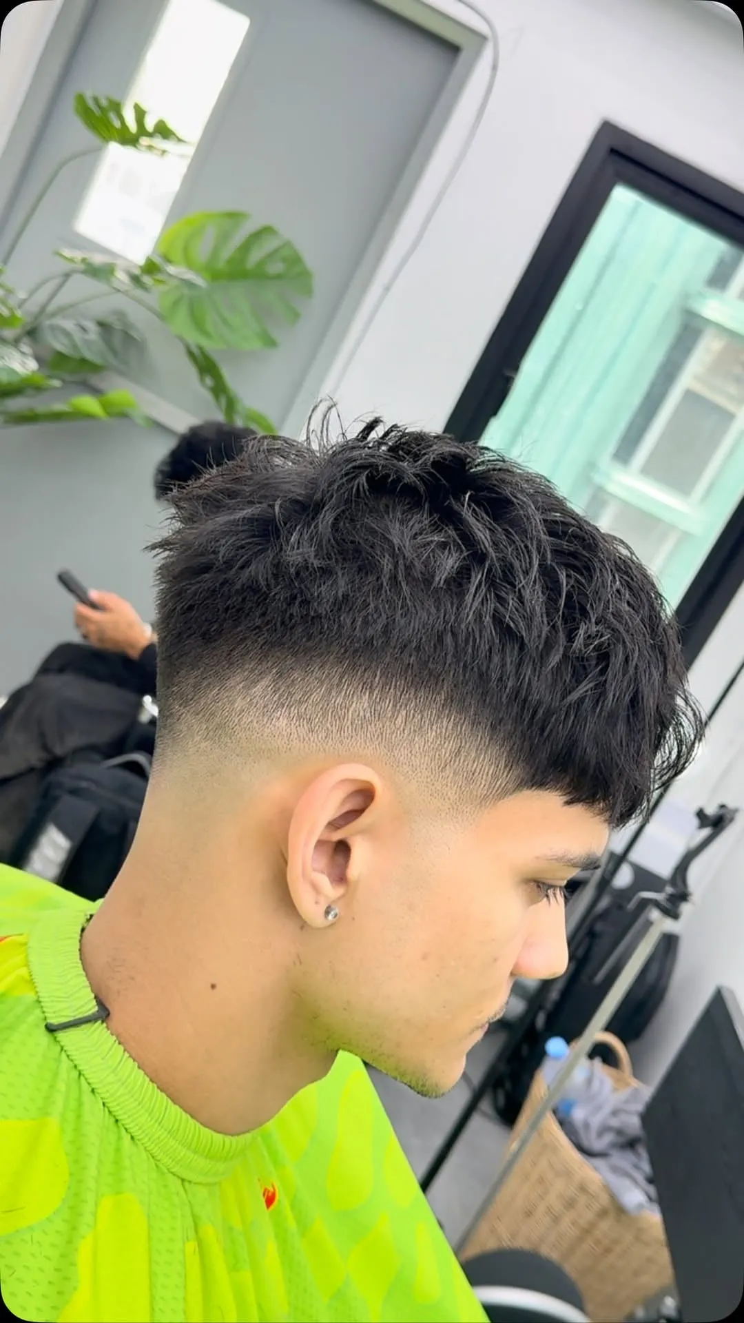 Joven de perfil con french crop negro, fleco largo y desfilado que cae sobre los ojos y drop fade que baja detrás de la oreja