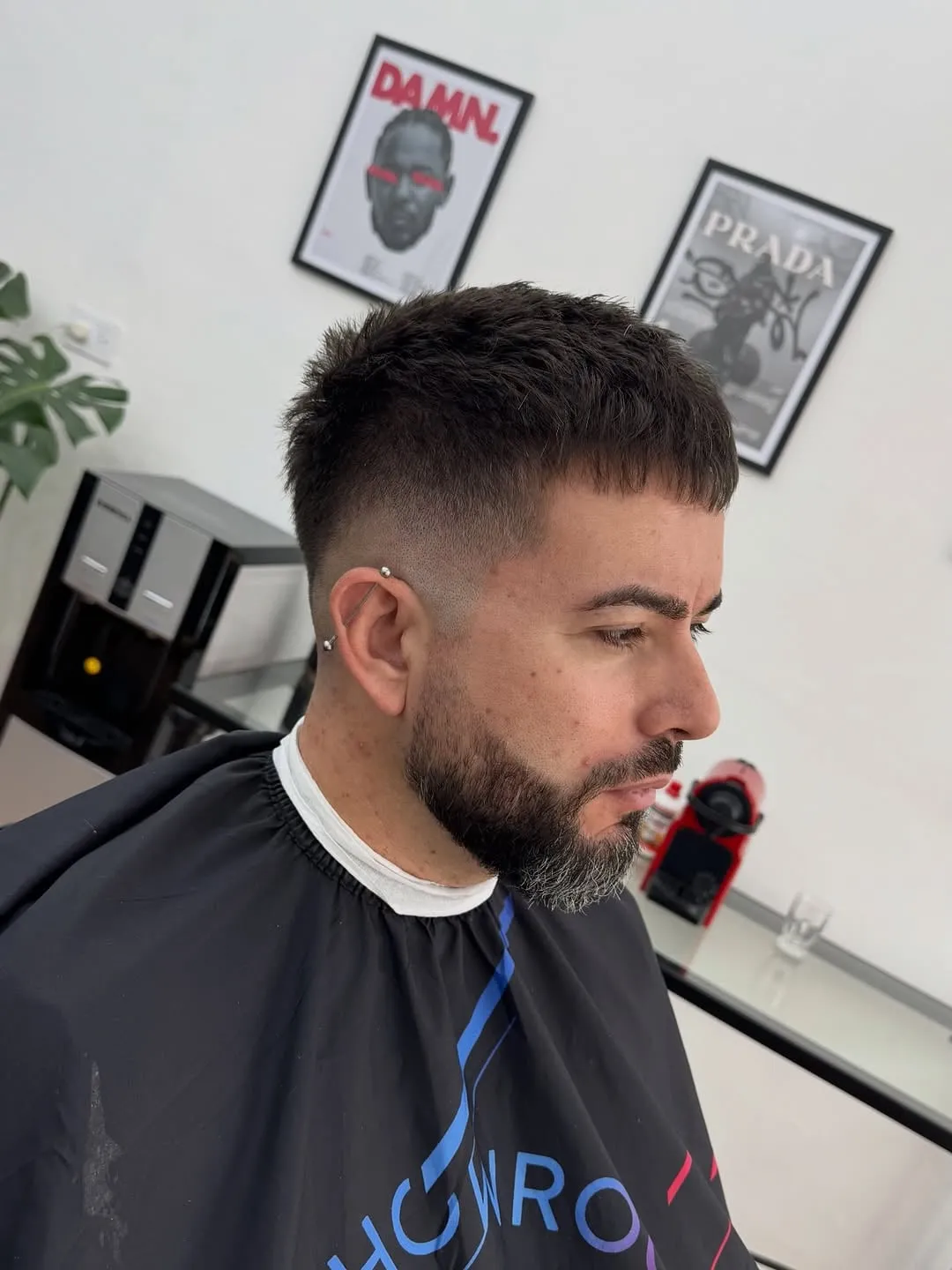 Hombre adulto con barba entrecana y french crop corto negro, fleco corto texturizado y mid fade en la barbería