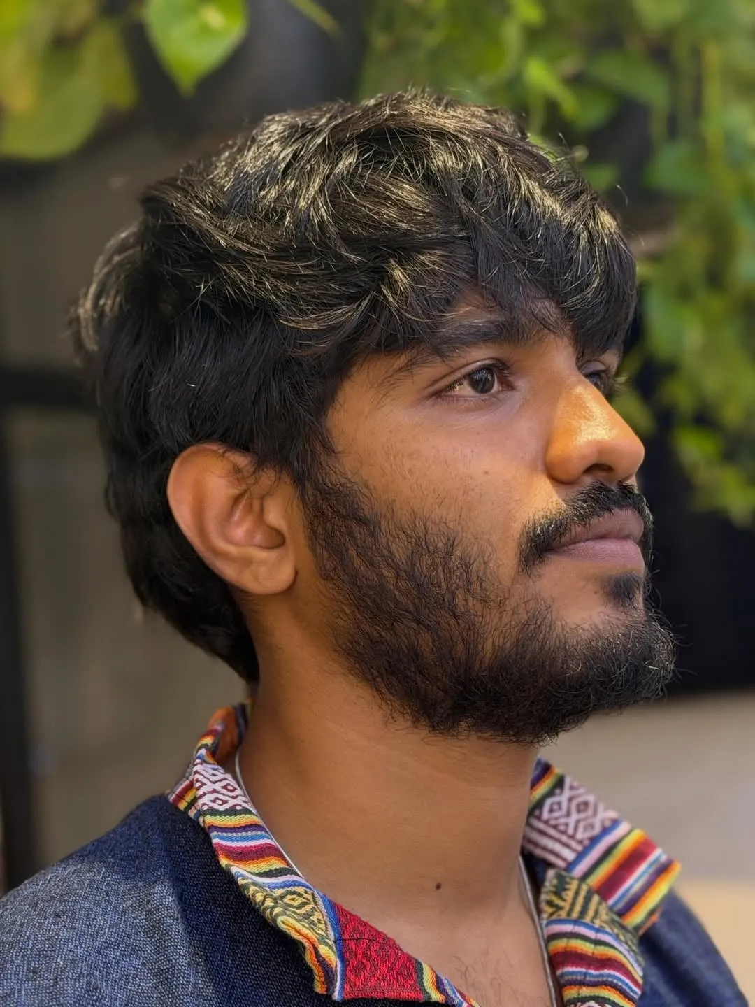 Hombre con barba y french crop largo en cabello negro ondulado, fleco desfilado a la altura de las cejas y lados cortos