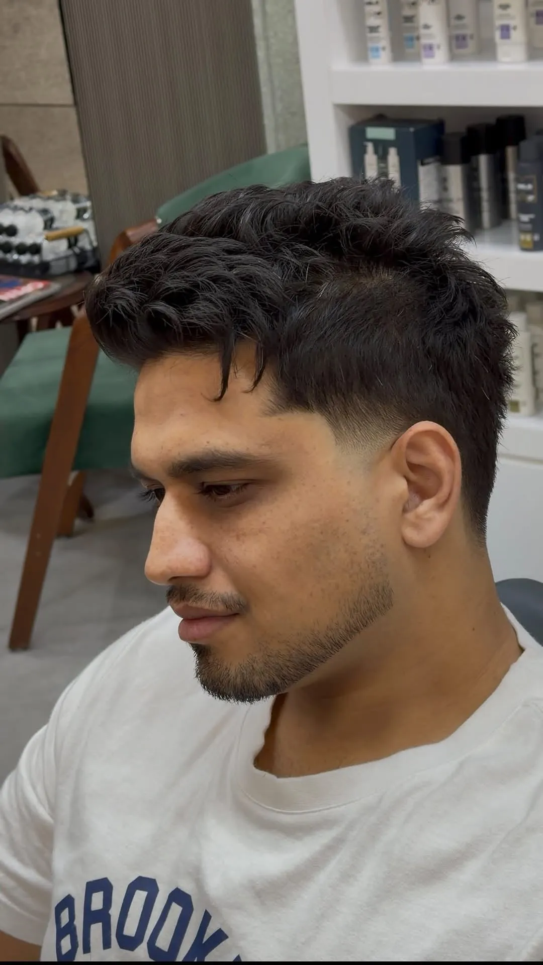 Hombre joven con french crop en cabello negro ondulado, fleco que cae hacia un lado de la frente y fade bajo