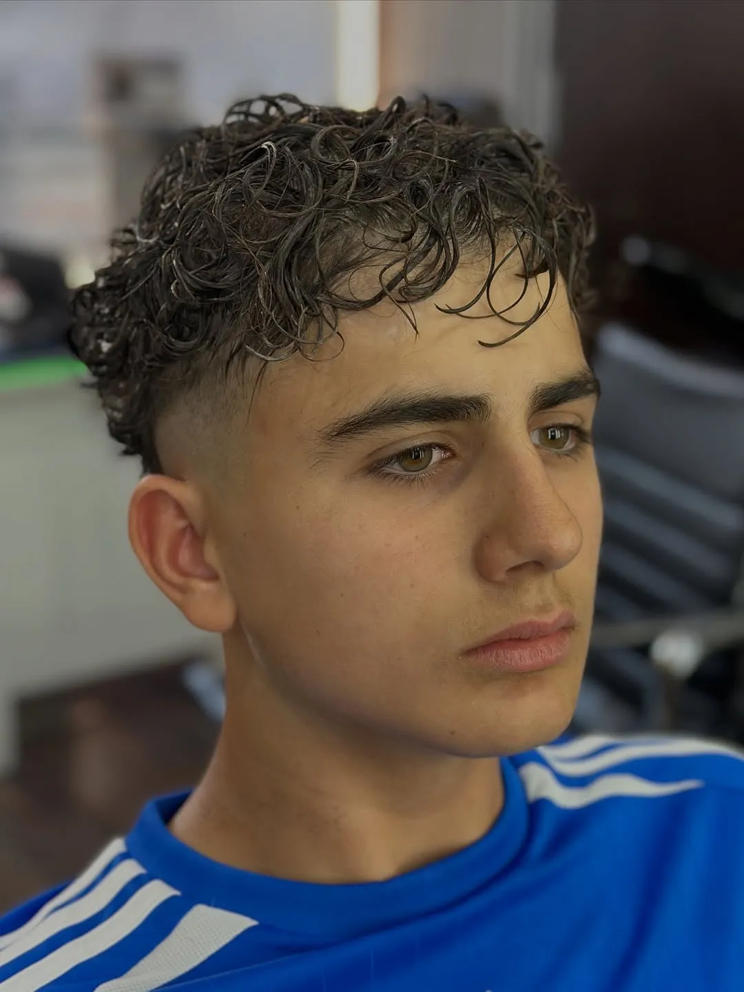 Joven con french crop de rizos sueltos castaño oscuro, unos 7 cm arriba, rizos sobre la frente y mid fade a los lados