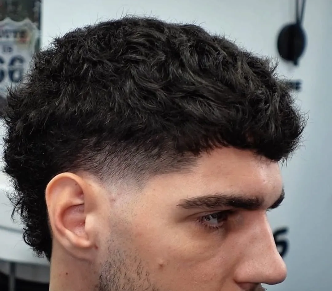 Hombre de perfil con French crop rizado, fleco corto y taper bajo en la sien