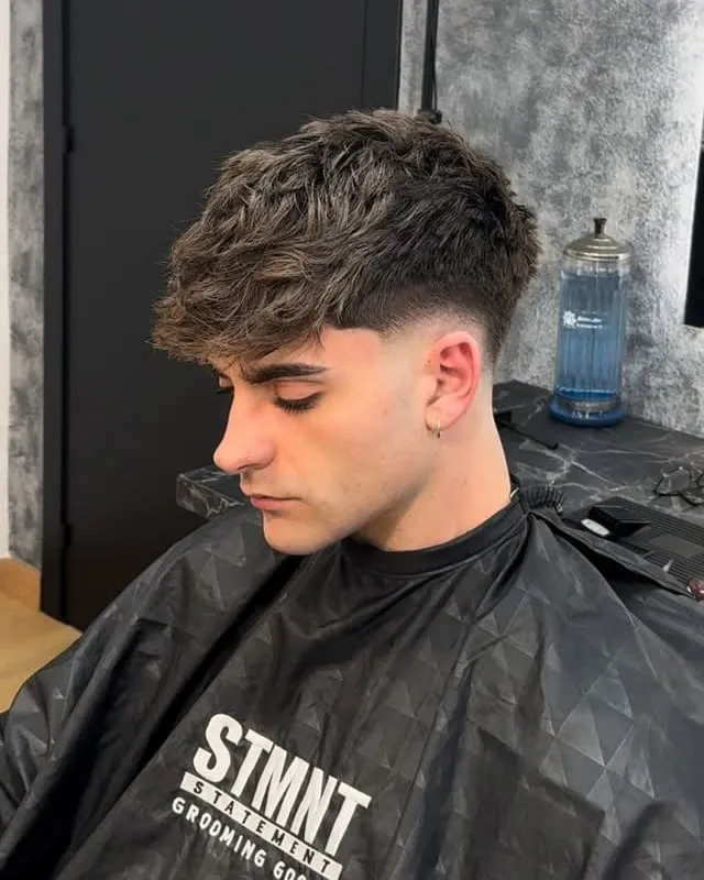 Joven con fleco largo con volumen y textura, low fade en los lados, sentado en barbería