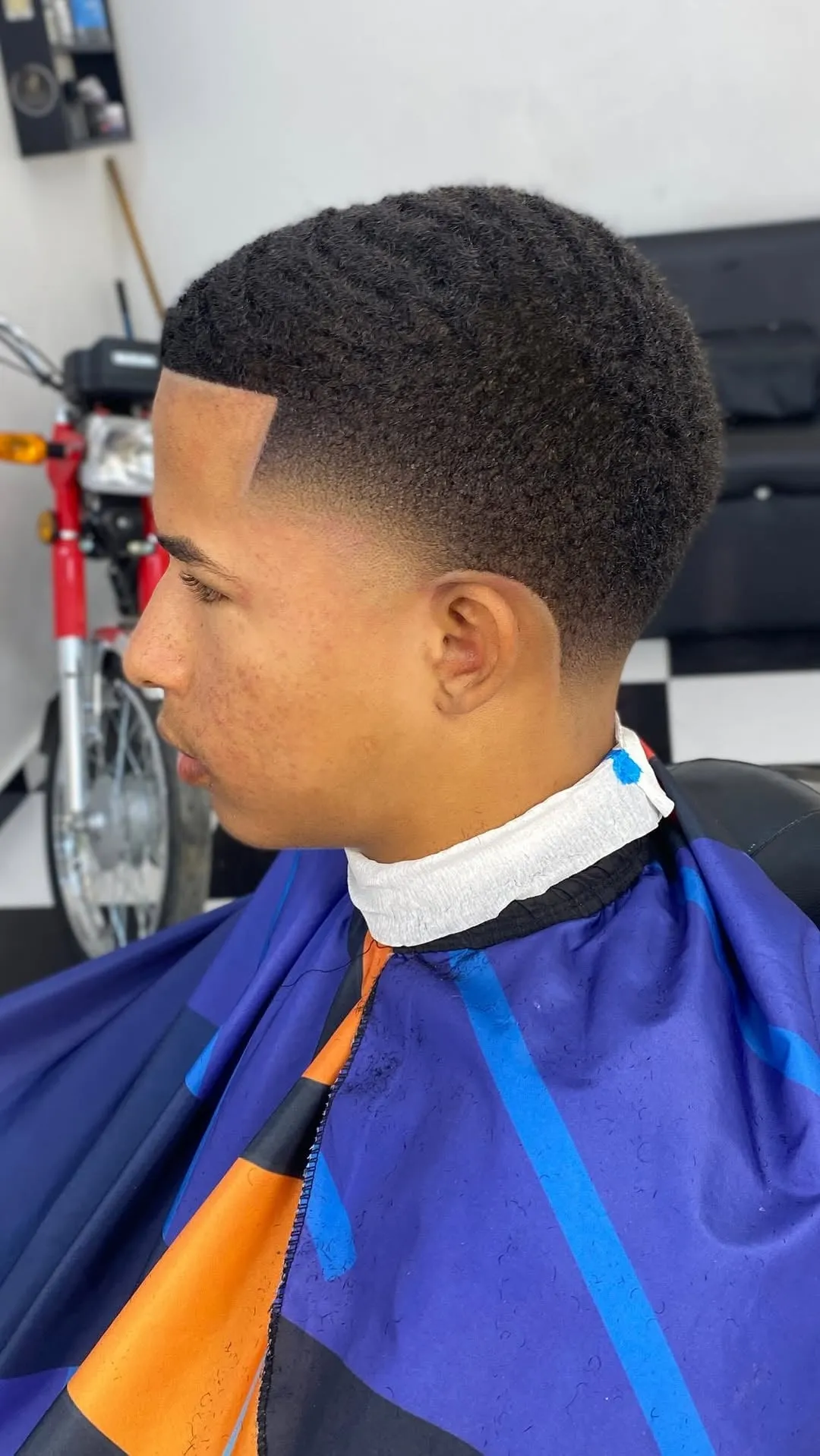 High taper fade en cabello afro corto con ondas y contorno marcado en la frente