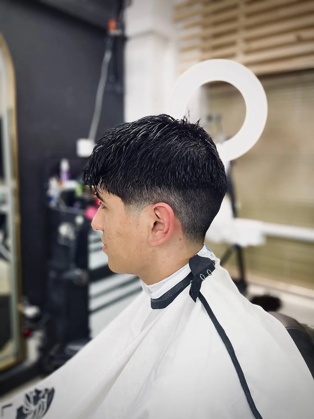 Low taper fade en cabello lacio negro con flequillo corto y patilla desvanecida
