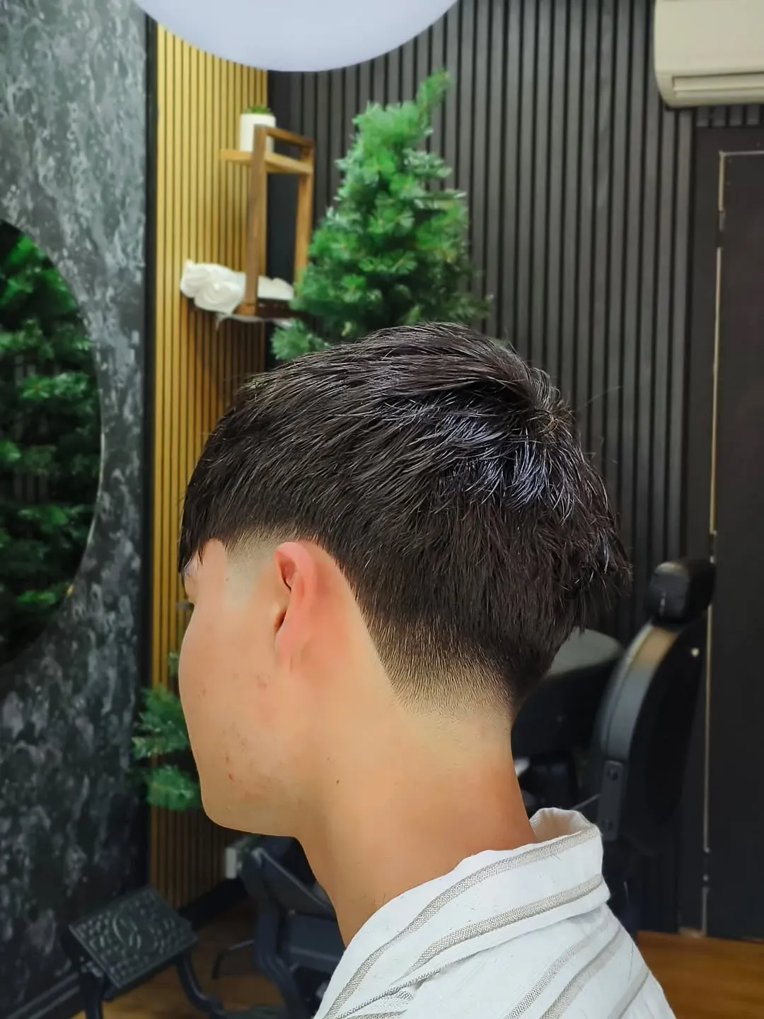 Mid taper fade de perfil con el desvanecido a media altura y cabello oscuro texturizado arriba