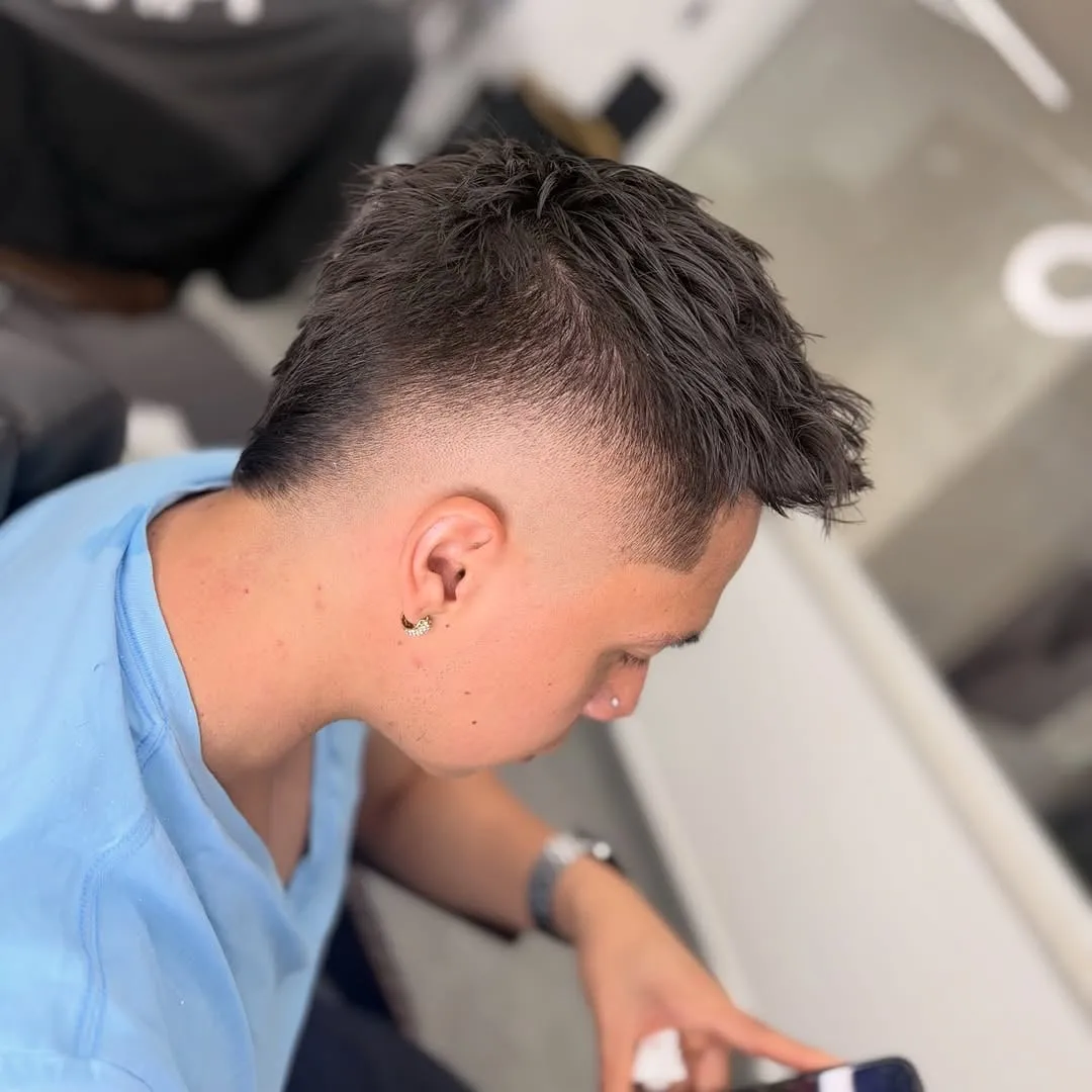 Hombre de perfil con mohawk fade de puntas texturizadas y degradado en las sienes, sentado en una barbería