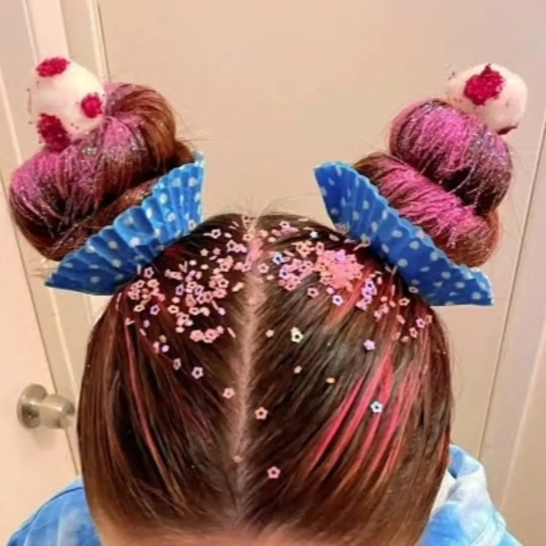 Niña vista desde arriba con dos chongos rosas decorados como cupcakes, capacillos azules y chispas de colores
