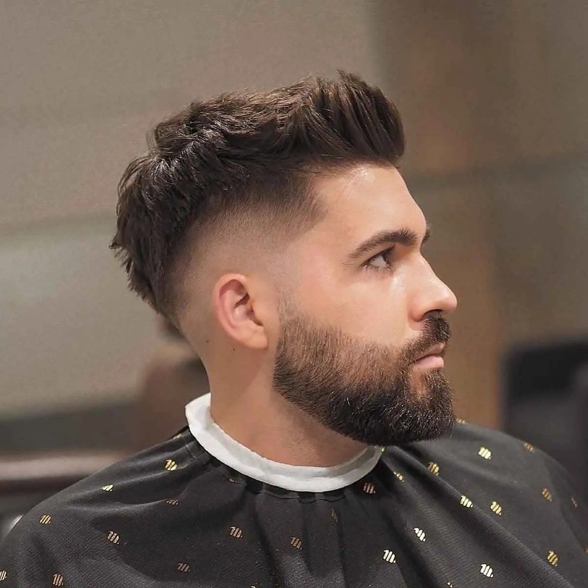 Hombre de perfil con quiff texturizado hacia el frente, desvanecido bajo y barba completa recortada