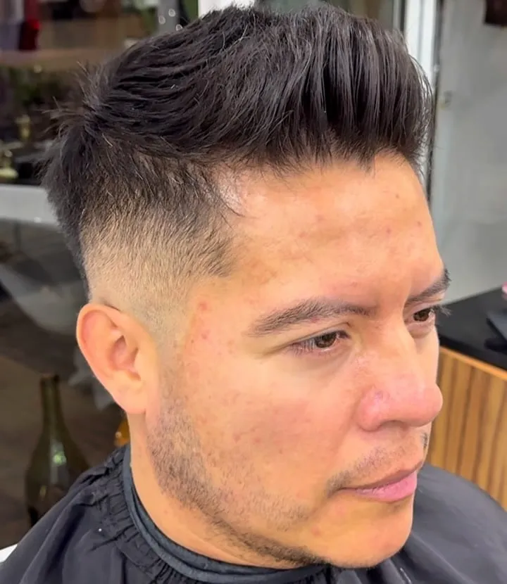 Hombre con quiff texturizado y desvanecido medio, cabello negro grueso peinado hacia arriba