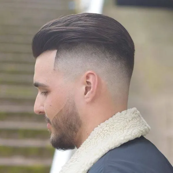 Hombre de perfil con pelo peinado hacia atrás tipo slick back, bald fade alto y barba recortada