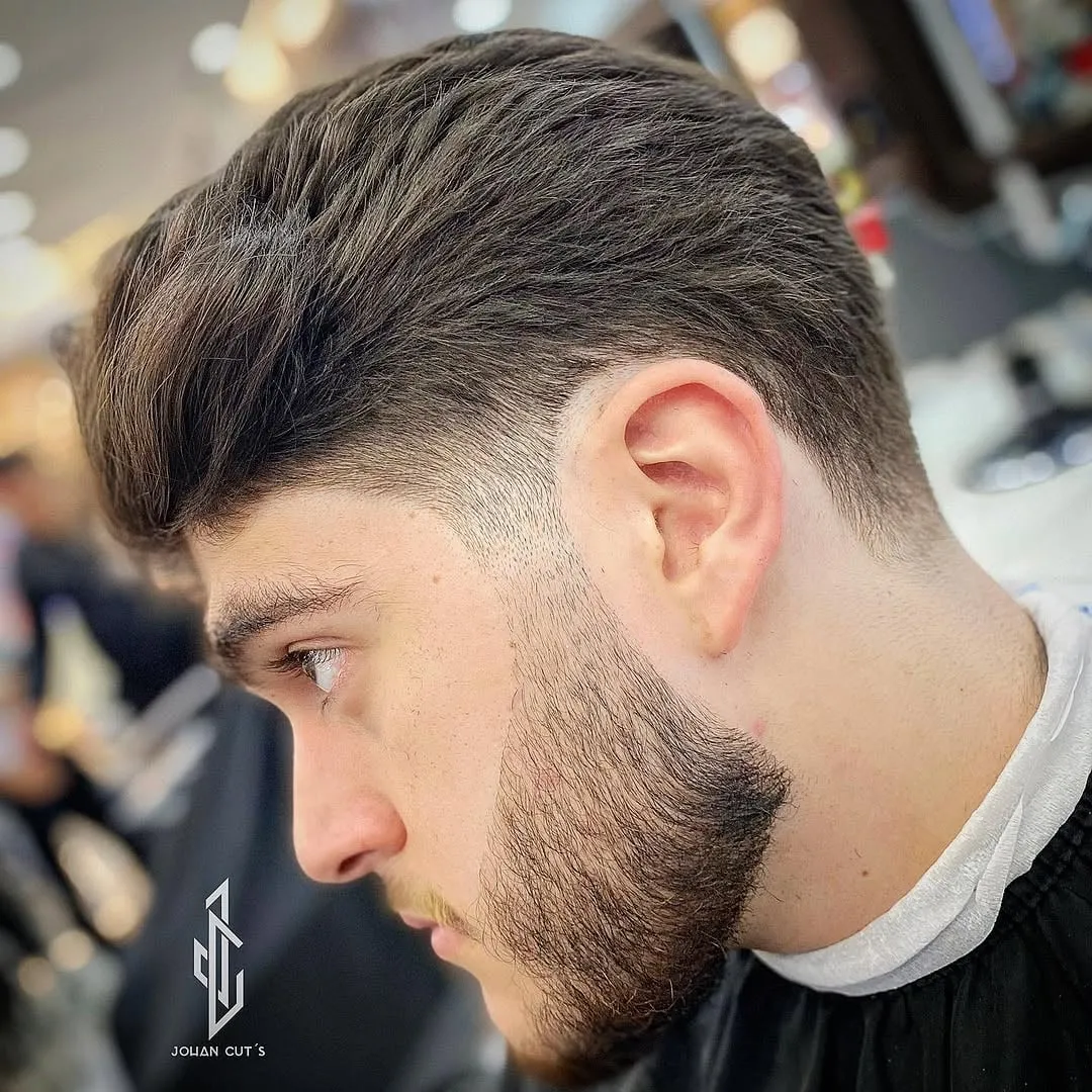 Taper fade unido a la barba con el cabello peinado hacia atrás y barba corta perfilada