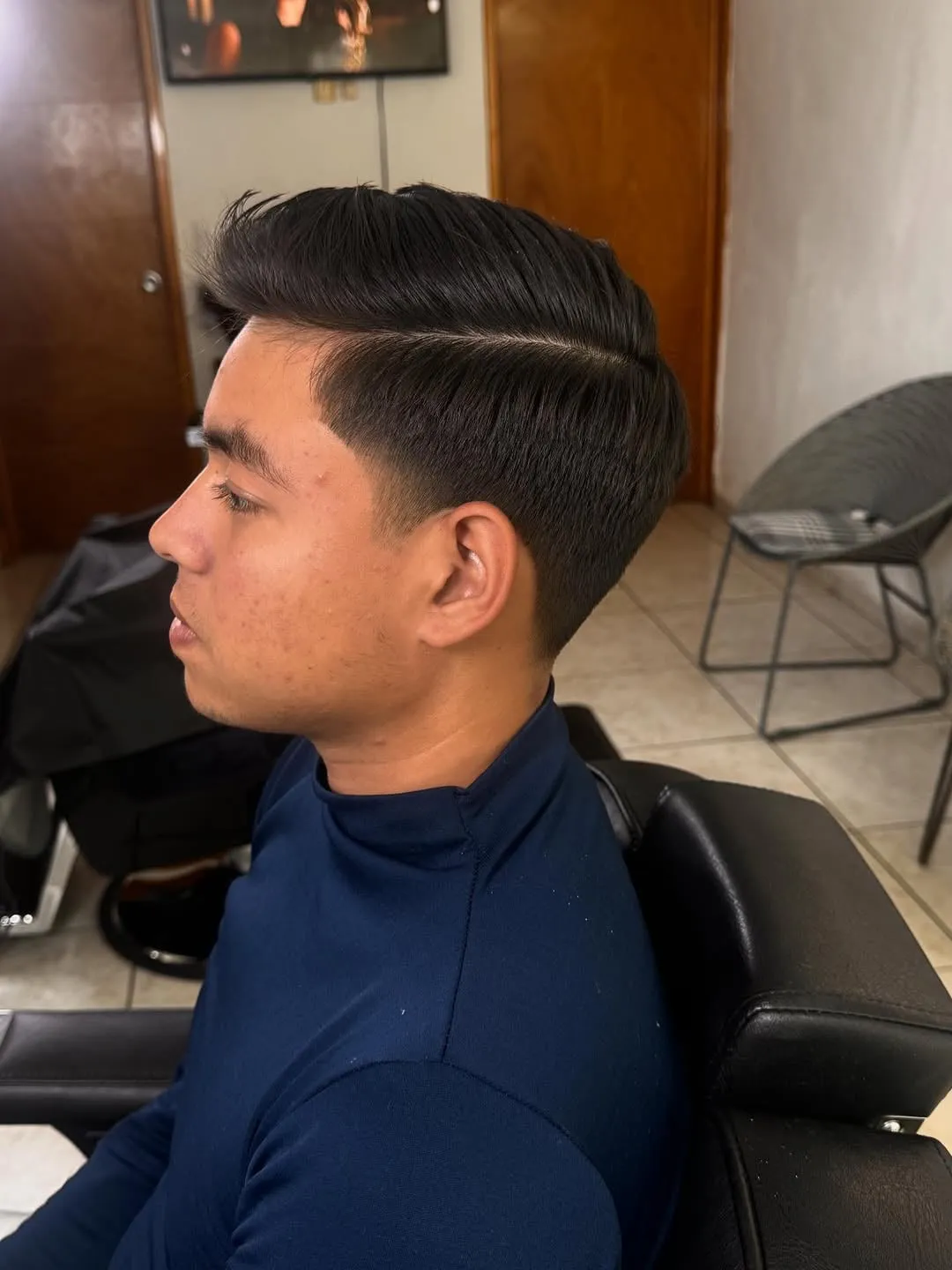 Taper fade bajo con raya marcada al costado y cabello negro peinado hacia un lado
