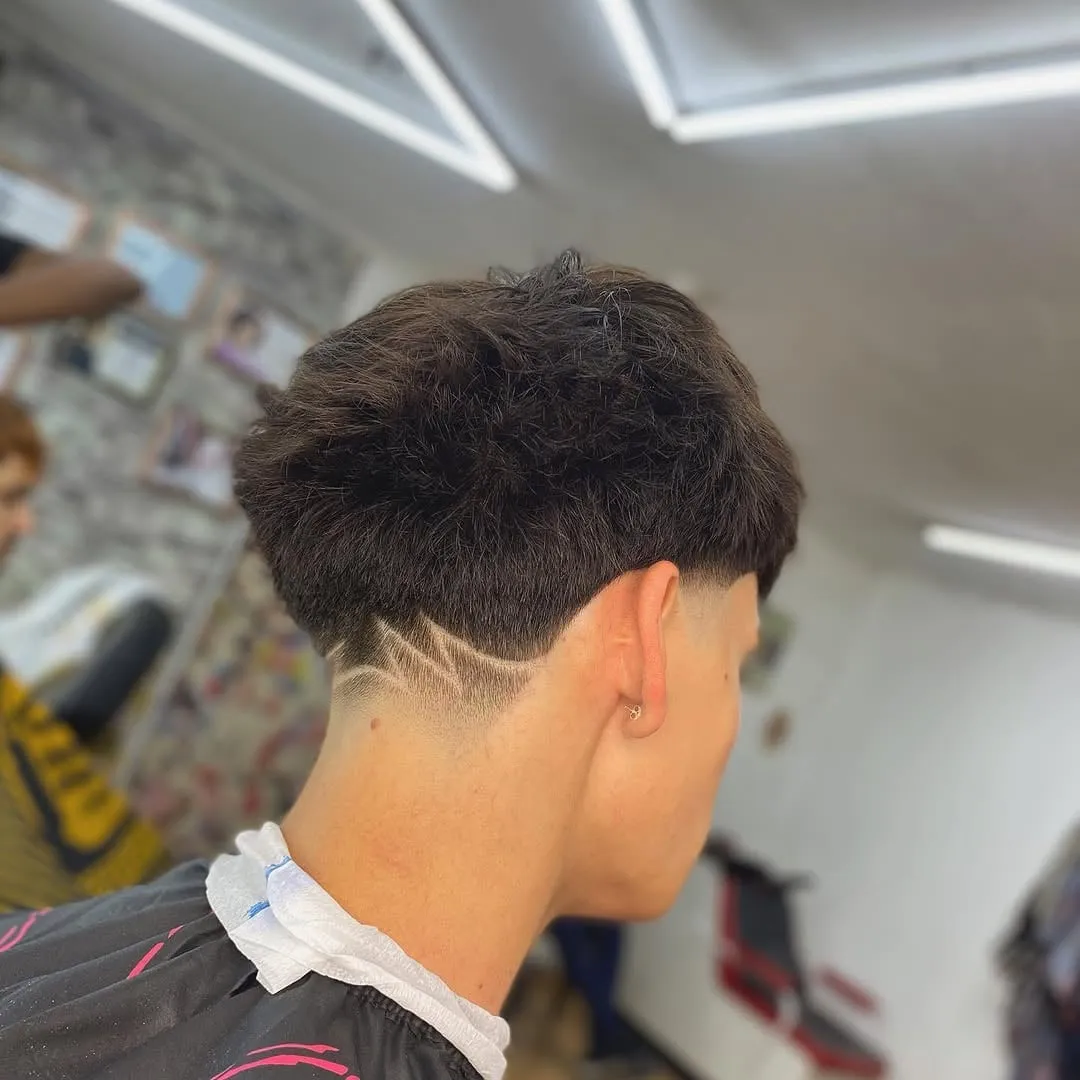 Taper fade bajo visto de espaldas con un diseño de líneas en la nuca y cabello texturizado arriba