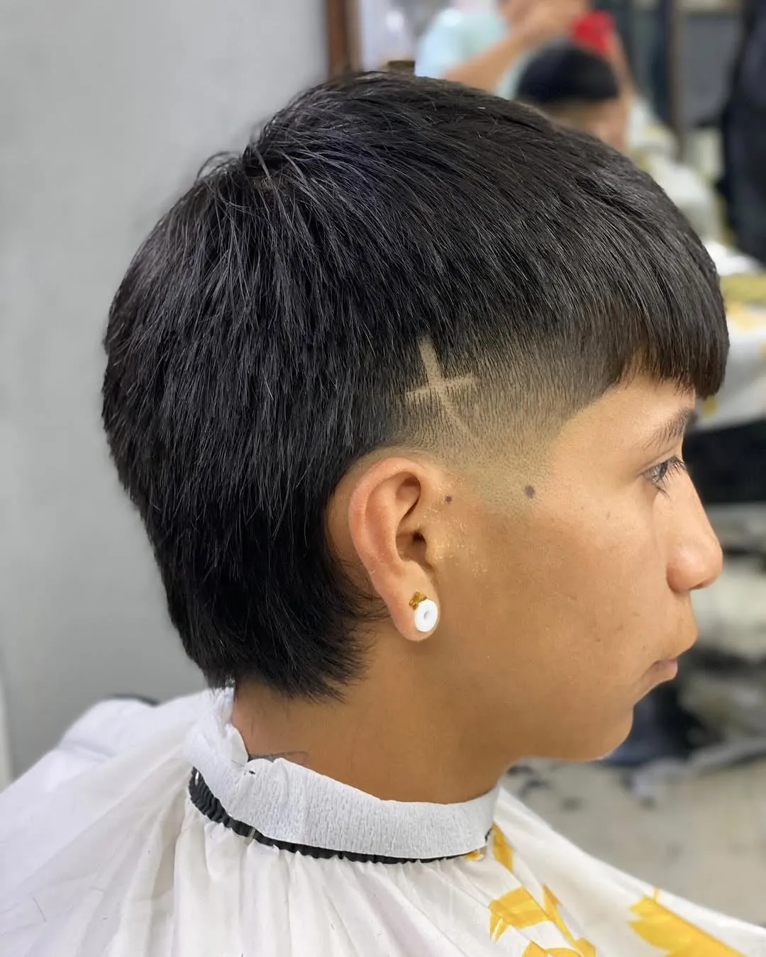 Taper fade con diseño de cruz al lado de la patilla y cabello negro lacio con fleco