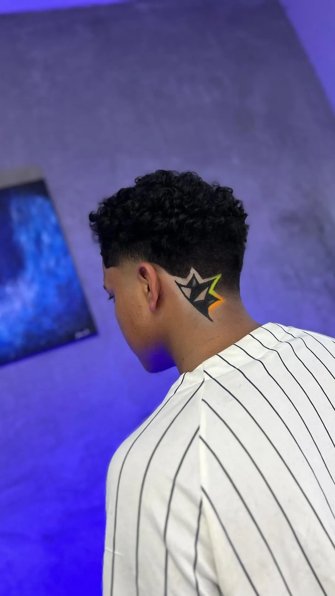 Taper fade en cabello rizado negro con una estrella grande en la nuca rellena de negro y bordes en amarillo y naranja