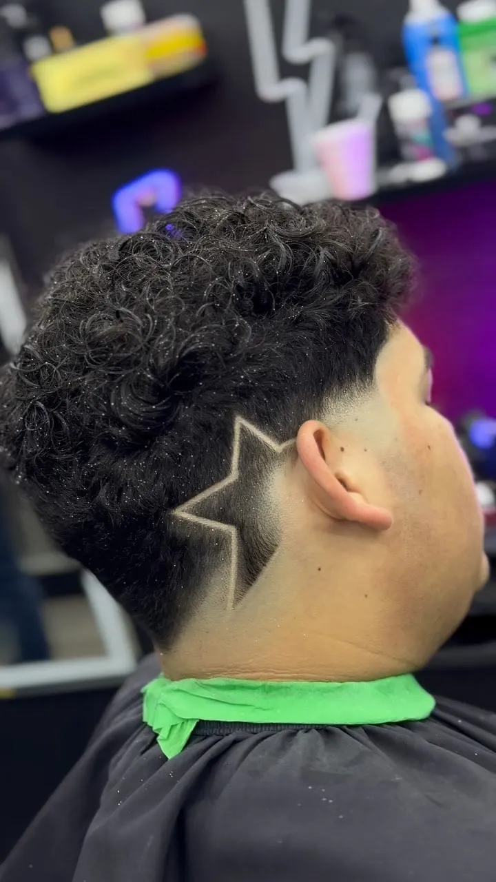 Taper fade en cabello rizado con diseño de estrella detrás de la oreja