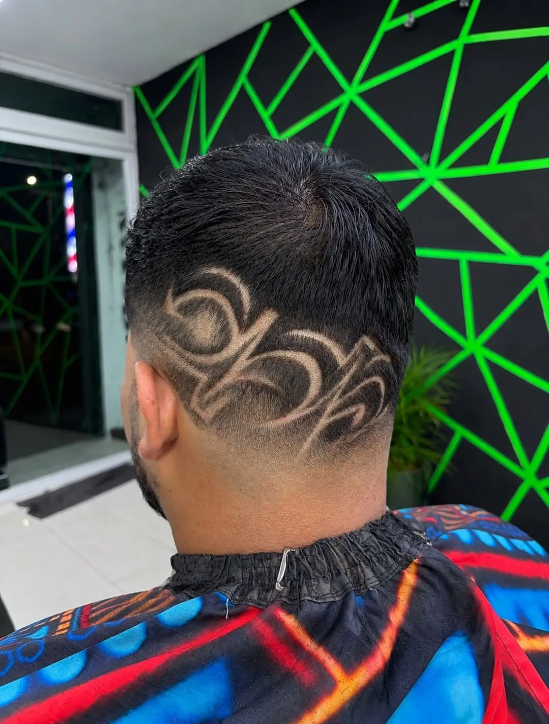 Taper fade visto de espaldas con un diseño freestyle de curvas entrelazadas en la nuca y cabello negro lacio corto