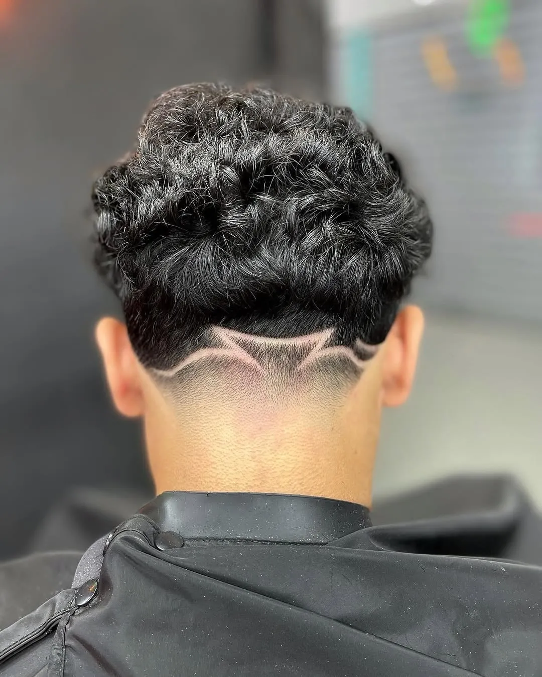 Taper fade visto de espaldas con diseño de líneas curvas en la nuca y cabello ondulado arriba