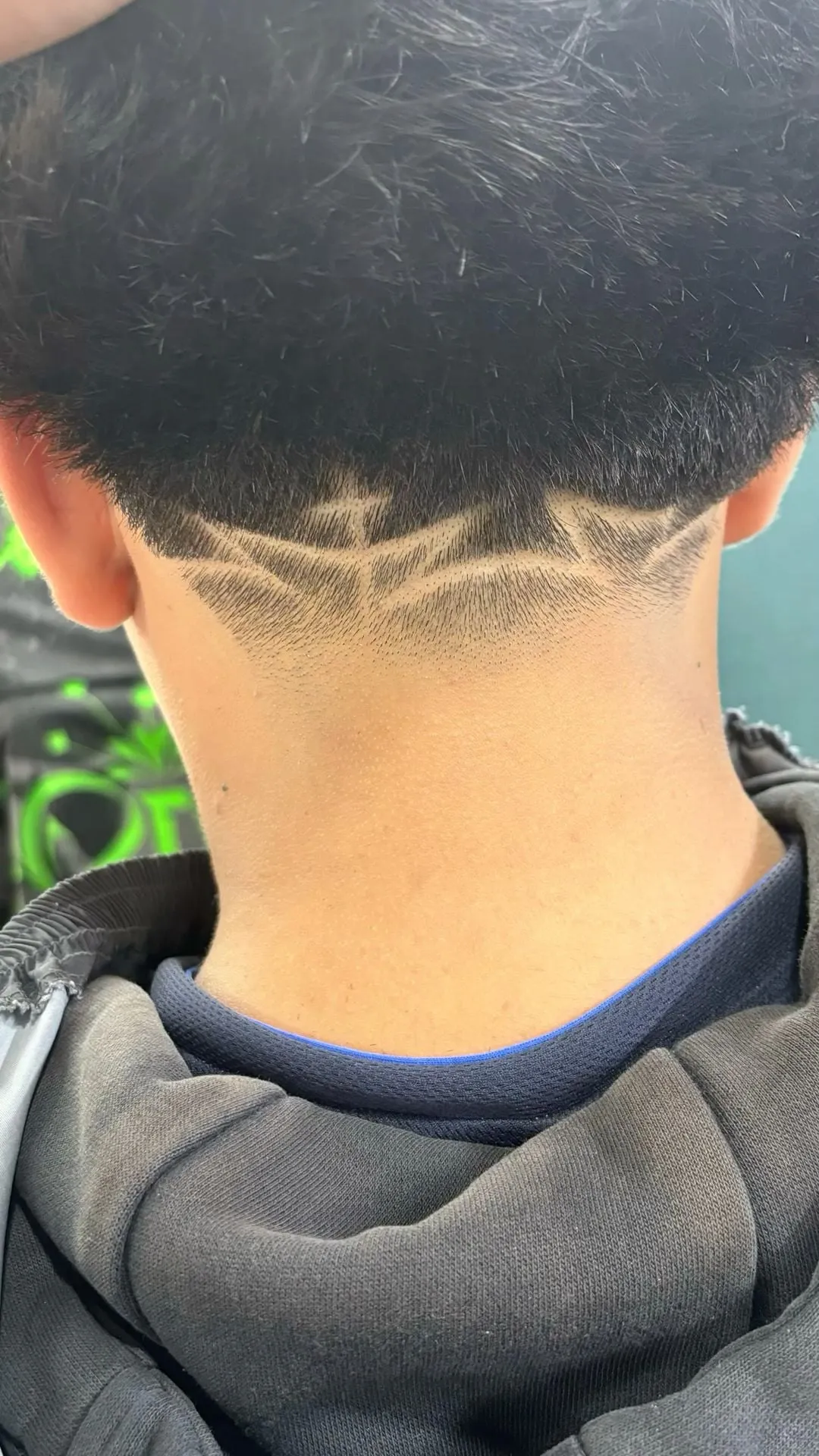 Taper fade visto de espaldas con líneas rectas en ángulo que forman un diseño simétrico en la nuca