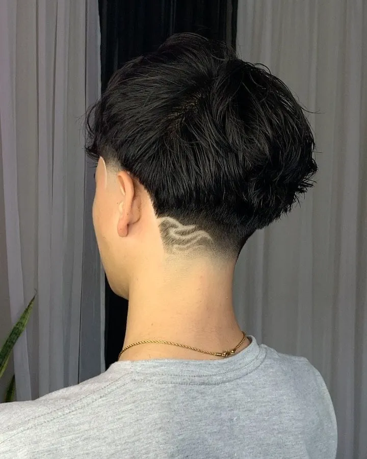 Taper fade bajo visto de espaldas con un diseño de llamas minimalistas en la nuca y cabello negro ondulado arriba