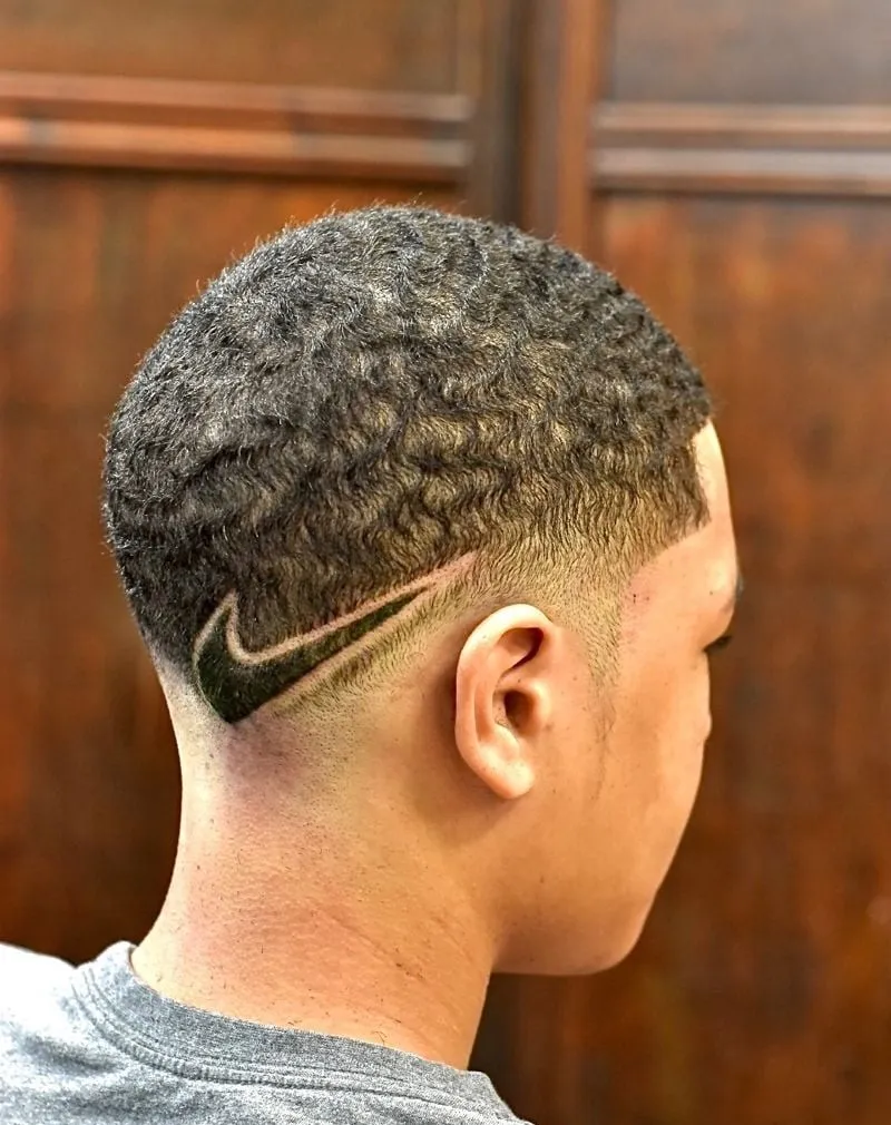 Low taper en cabello afro corto con ondas y un logo de Nike relleno dibujado detrás de la oreja