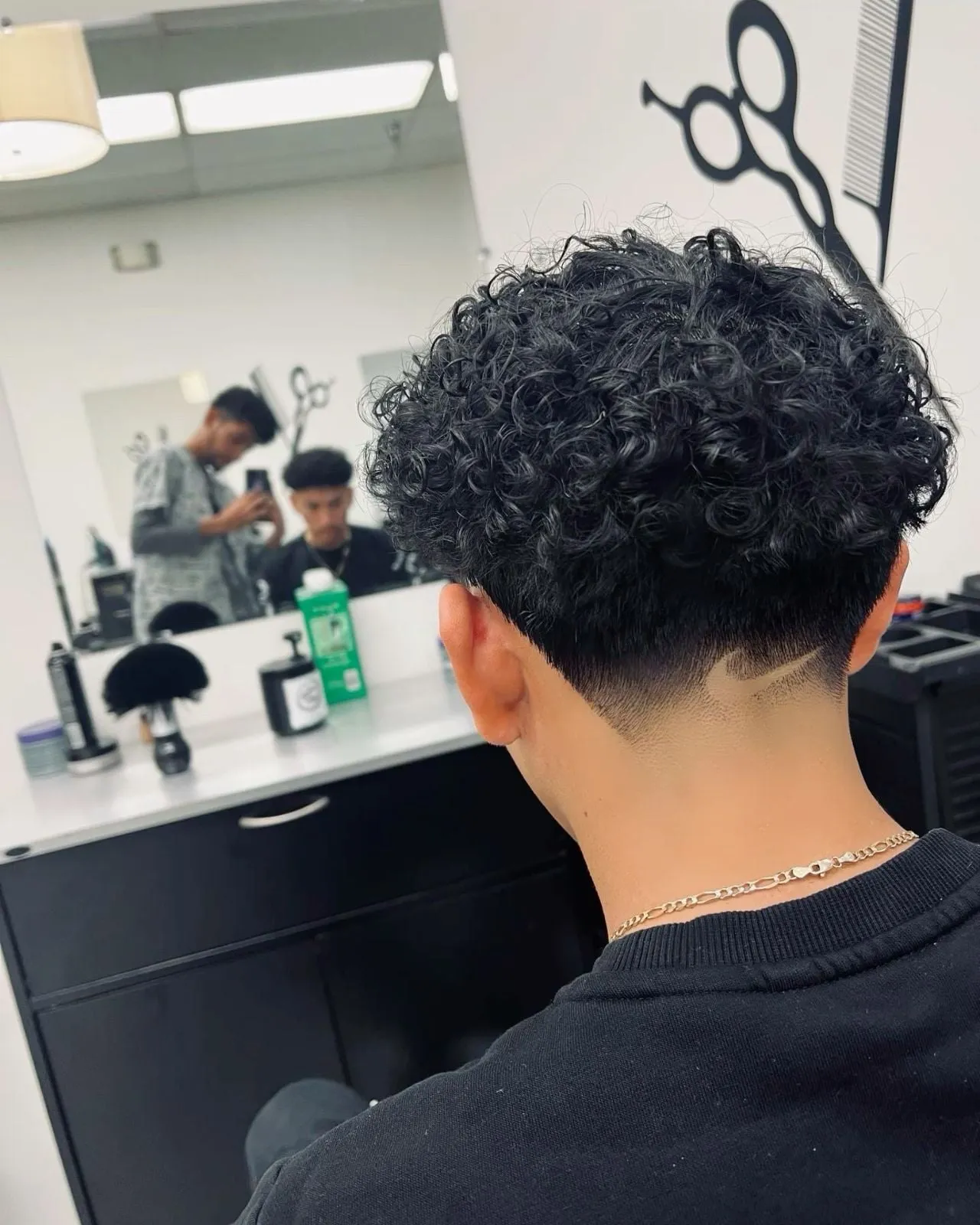 Taper fade en cabello rizado negro visto de espaldas con un pequeño diseño Nike en la nuca