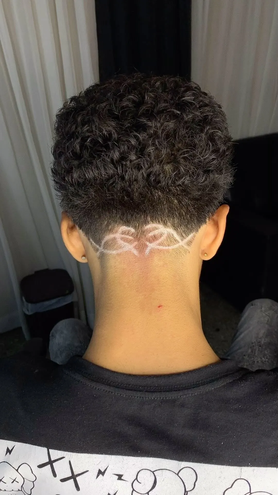 Taper fade en cabello rizado visto de espaldas con un diseño de ondas marcado en blanco en la nuca