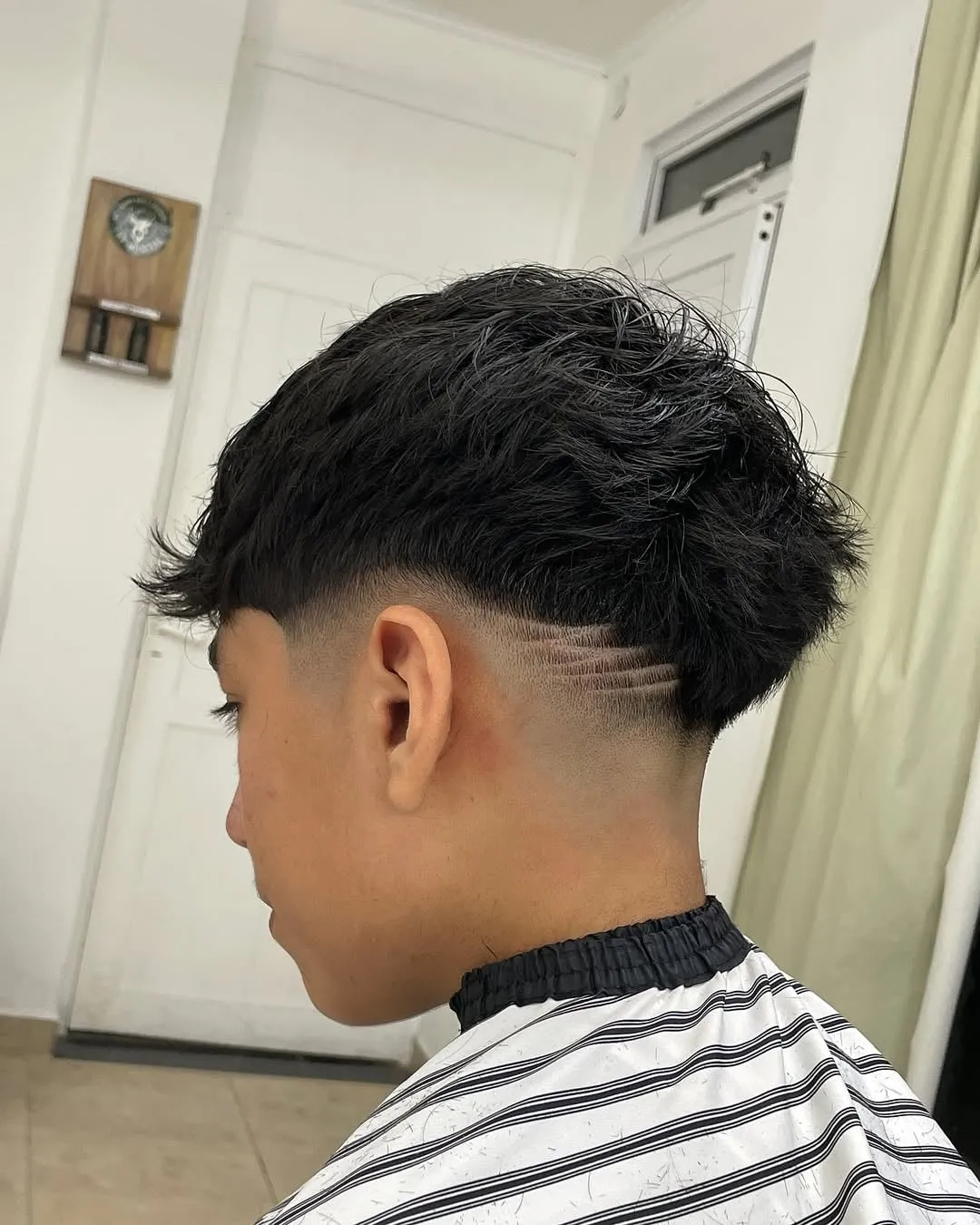 Taper fade en cabello negro lacio texturizado con tres rayitas paralelas detrás de la oreja