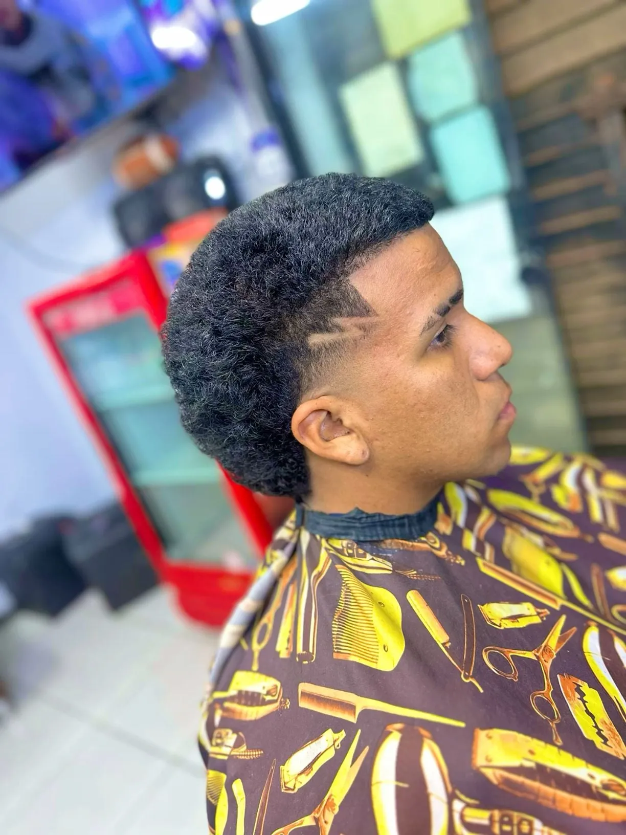 Taper fade alto en cabello afro corto con un rayo pequeño dibujado en la sien sobre la patilla